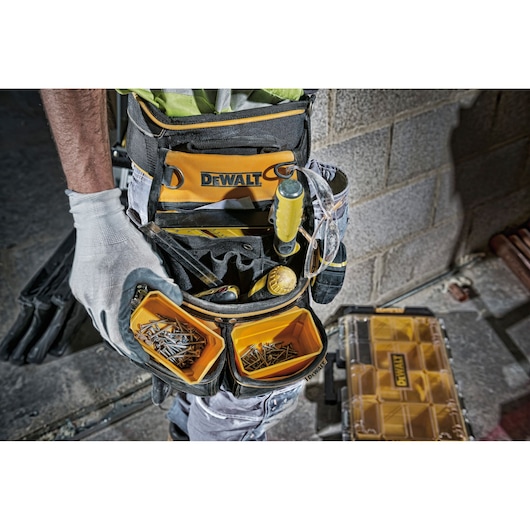 A DEWALT tool belt worn by a worker, showing various tools and two compartments filled with nails, screws, and small