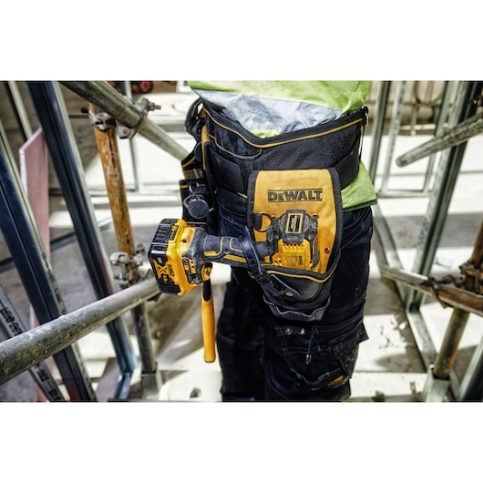 A close-up of a construction worker wearing a DEWALT branded tool belt with a yellow cordless power tool holstered on the