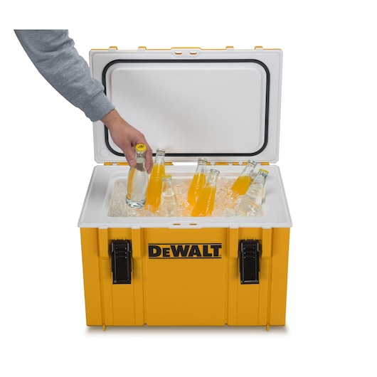 A yellow DEWALT cooler with a white lid is open, filled with ice and several glass bottles. A person's hand is reaching into the cooler, picking up one bottle.