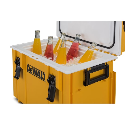 A yellow DEWALT cooler box with its lid open, containing six glass bottles of orange and red beverages placed in ice.