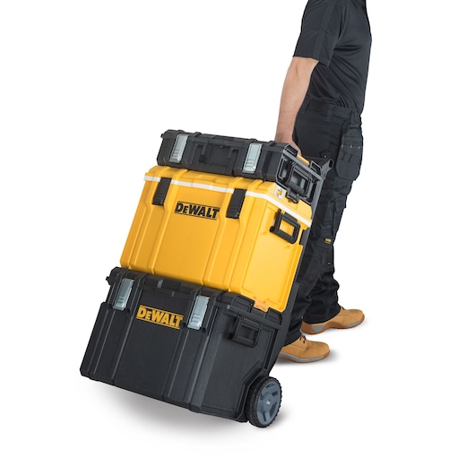 A person is pulling a stack of DEWALT branded tool storage boxes on wheels. The boxes are black and yellow and securely latched together for easy transport.