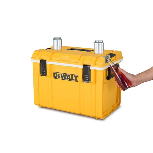A yellow DEWALT cooler box with black latches, featuring two cans on top and a bottle being opened using the built-in bottle opener on the front right side.