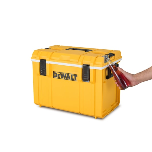 A yellow DEWALT storage box with a DEWALT logo on the front. A hand is using a bottle opener built into the box to open a glass bottle.