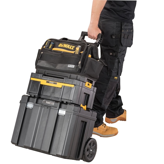 Person pulling DEWALT TSTAK rolling tool storage stack with black and yellow boxes and bag.