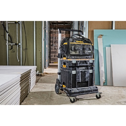 A DEWALT rolling tool storage system with multiple stacked toolboxes and a tool bag on top, situated in a construction site
