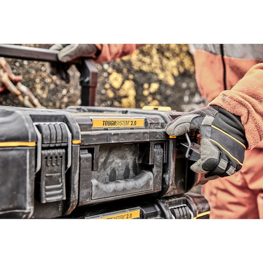 Gloved hand unlocking a DEWALT TOUGHSYSTEM 2.0 tool box outdoors, close-up of handle and latch.