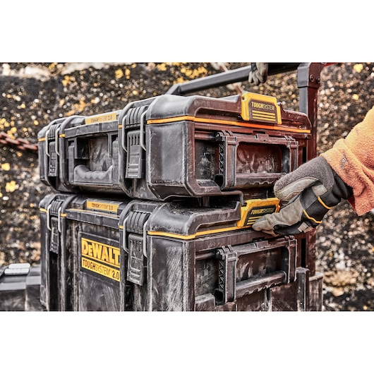 Stacked DEWALT ToughSystem 2.0 toolboxes with a gloved hand adjusting the latch outdoors.