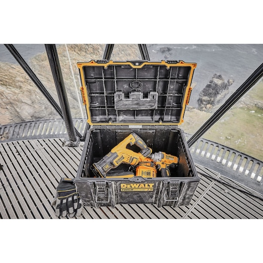 A DEWALT ToughSystem 2.0 tool box with its lid open, containing two cordless DEWALT power tools and a pair of gloves placed
