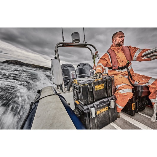 A person wearing an orange safety suit sits on a speedboat with two DEWALT storage boxes in front. The boat is moving fast