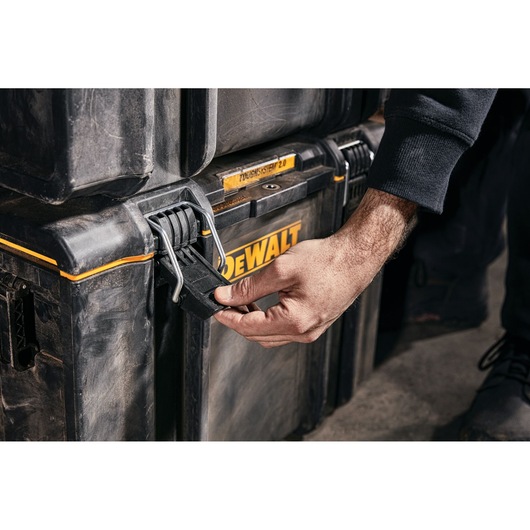 Hand opening latch on a DEWALT ToughSystem 2.0 storage box in a workshop setting.