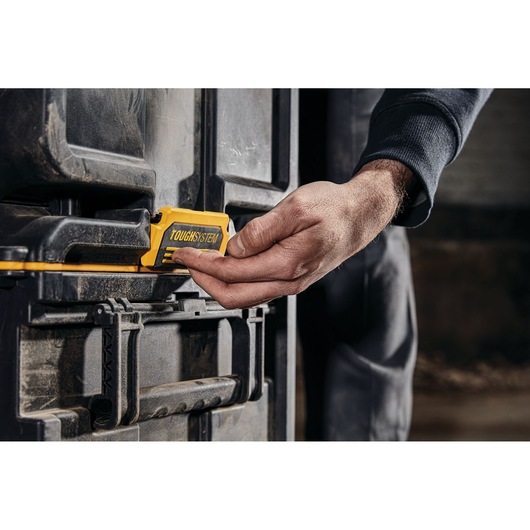 Hand operating the yellow TOUGHSYSTEM latch on a DEWALT storage box in a workshop setting.