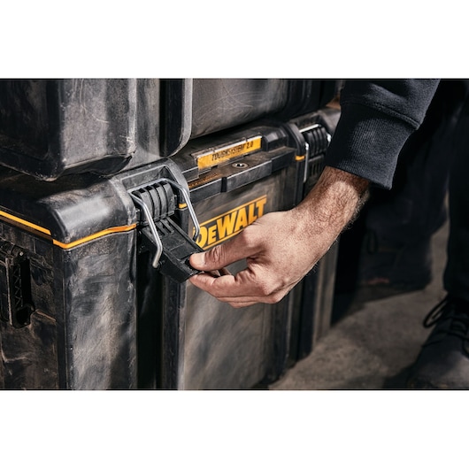 Hand unlocking a DEWALT ToughSystem 2.0 storage box latch, close-up view of rugged black toolbox.