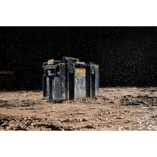 A DEWALT DWST83342-1 tool storage box covered in mud and water, placed on a muddy surface with water droplets splashing