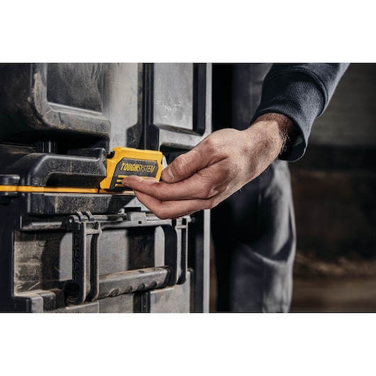 Hand unlatching a DEWALT TOUGHSYSTEM toolbox, showing the yellow latch on a rugged black case.