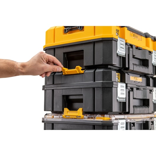 Hand unlocking stacked DEWALT TSTAK toolboxes with yellow latches and black bodies.