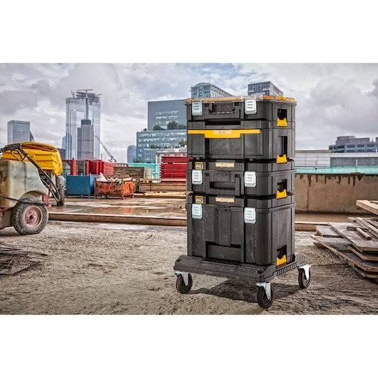 A stack of four black DEWALT tool storage boxes with yellow accents, mounted on a wheeled trolley, placed on a construction