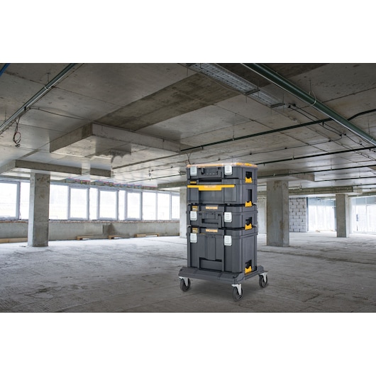 A stack of DEWALT portable tool storage boxes on a wheeled trolley positioned in an unfinished industrial building with