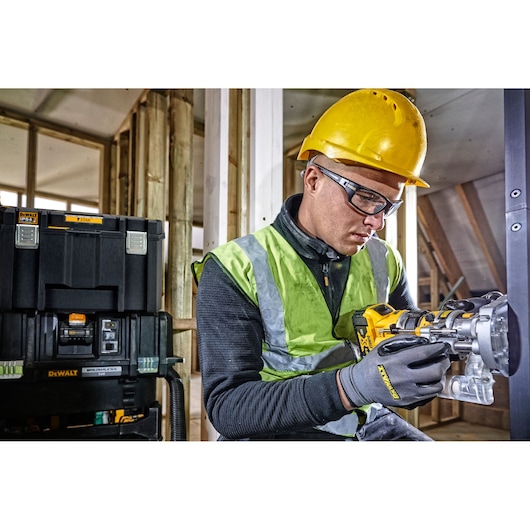 A construction worker wearing a yellow hard hat and a reflective safety vest is using a DEWALT power tool inside a building