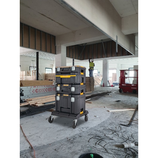 A stack of three DEWALT DWST83346-1 tool storage boxes on a rolling cart, placed in the middle of a construction site with