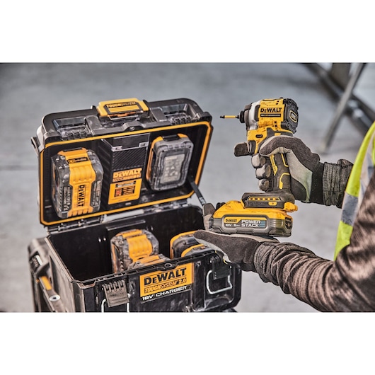 A person wearing gloves holds a DEWALT cordless power tool with a POWERSTACK 18V battery, next to an open DEWALT ToughSystem