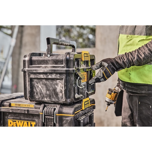 A person wearing work gloves operates a DEWALT ToughSystem 2.0 storage box, stacked on another DEWALT storage box, at a