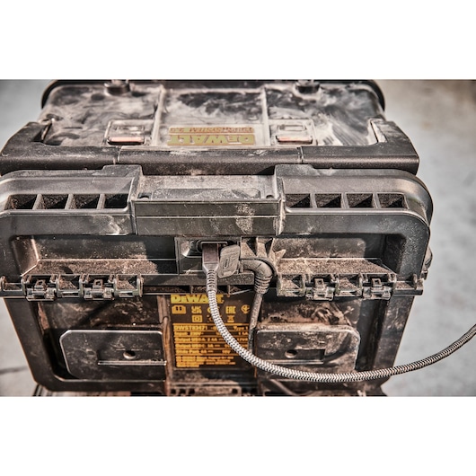 Dusty DEWALT tool box with cable plugged into the front, seen in close-up on a work site.