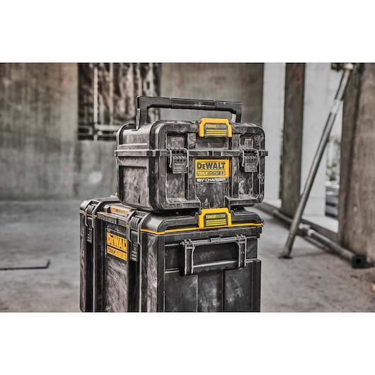 Three stacked DEWALT ToughSystem tool boxes in a construction site, showing durable black cases with yellow labels.