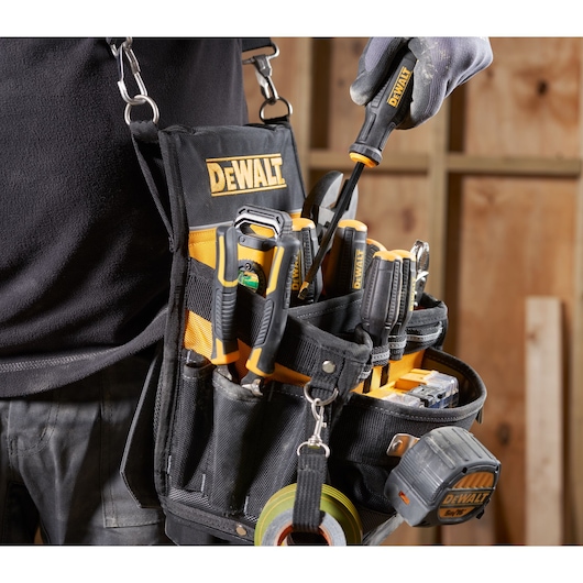A close-up of a DEWALT branded tool belt worn by a person, filled with various DEWALT hand tools, tape measure, and