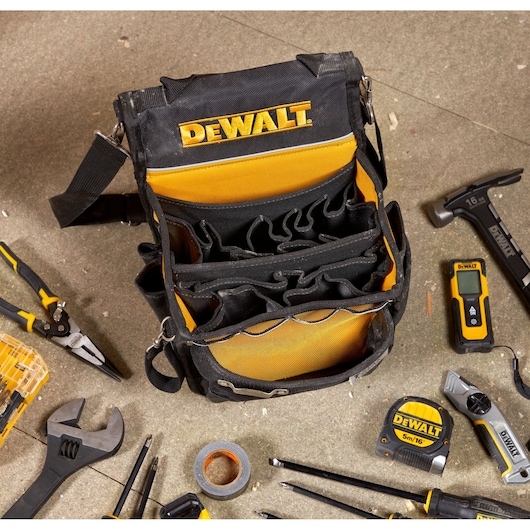 A DEWALT branded black and yellow tool bag with multiple compartments is displayed on a work surface, surrounded by various