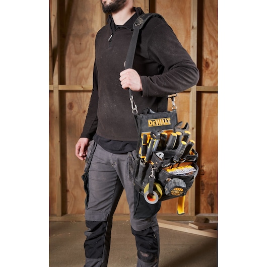 A person carrying a DEWALT tool organizer shoulder bag filled with various hand tools and tape. The scene is set in a