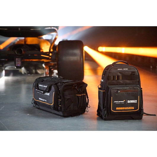 DEWALT McLaren special edition tool bag and backpack, shown beside a race car with orange lights in background.