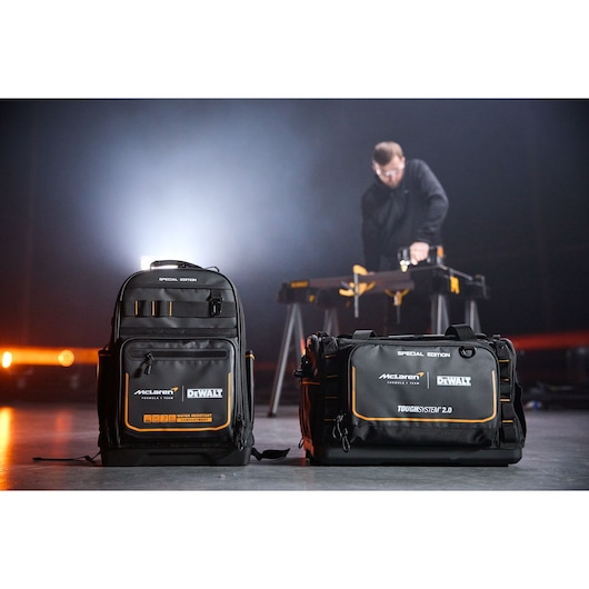 Two DEWALT McLaren tool bags are displayed on the floor, with a blurred person working in the background.