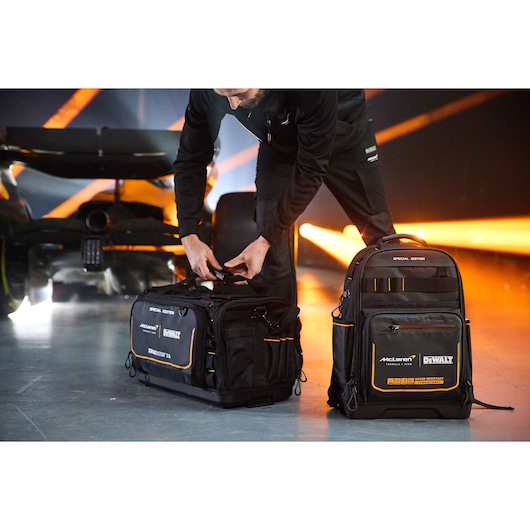 A person with DEWALT special edition tool bags near a race car; one is a duffel, one is a backpack.