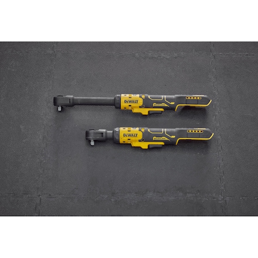 Two DEWALT cordless ratchets with yellow and black handles are placed side by side on a dark textured surface.