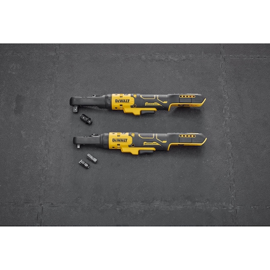 Two DEWALT cordless ratchets with attachments lie on a black textured surface, shown side by side.