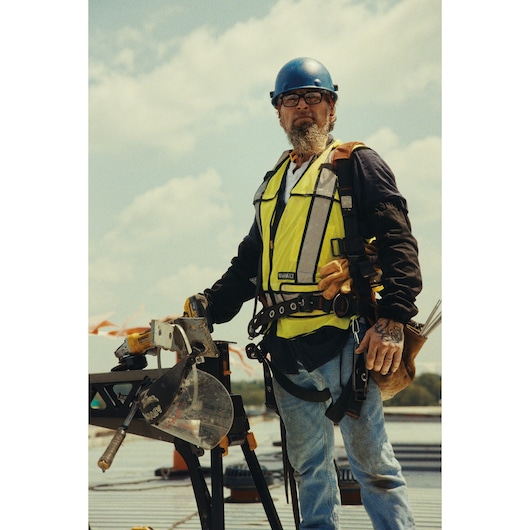 Worker with DEWALT saw models DCS782N, DCS782XW2 on site. Safety gear and tool belt visible.