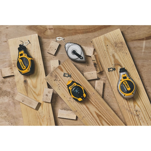 Several DEWALT chalk line reels and a metal chalk line reel are displayed on wooden boards with scattered sawdust and wood pieces.