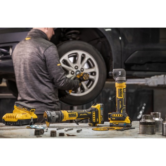 DEWALT tools DCG430E2T, DCG430N-XJ, DCG430N, DCG421N-XJ, DCG421N on a table in a garage, mechanic working on a car.