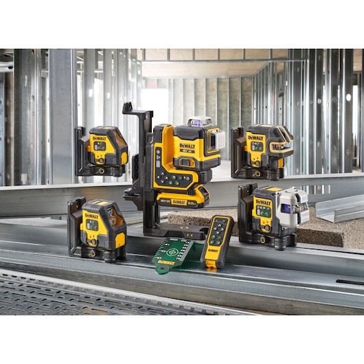 A collection of DEWALT laser levels and measuring tools displayed on a construction site, featuring metal framing in the background. The tools are yellow and black and are positioned on steel beams, with accessories including a remote control and laser target plate.