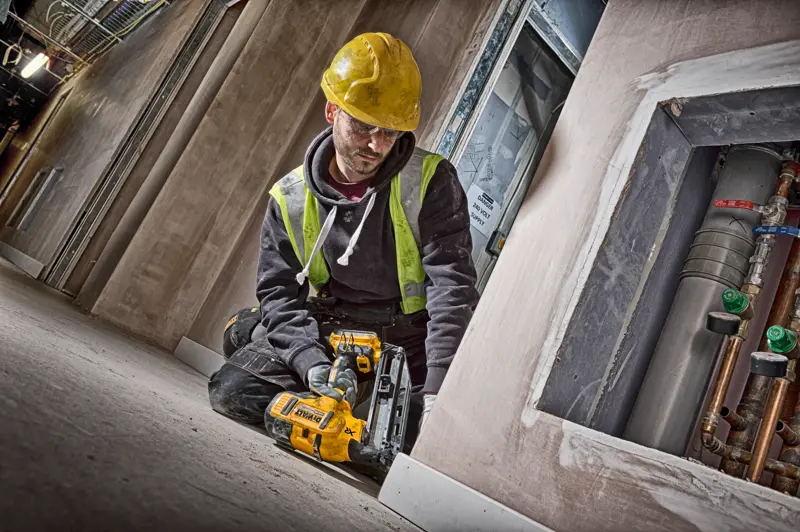 Worker using a DEWALT DCN660N nailer on a construction site, wearing a yellow hard hat and safety vest.