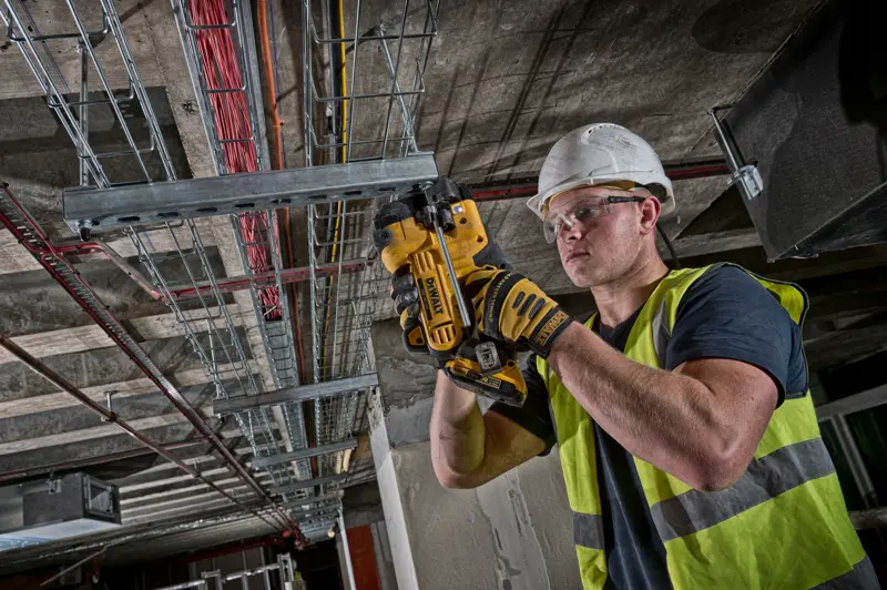 Worker using DEWALT DCS350NT tool to cut metal conduit on ceiling installation site.