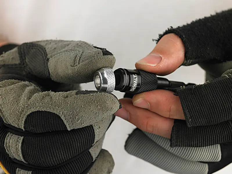Gloved hands holding and adjusting a DEWALT drill bit holder.